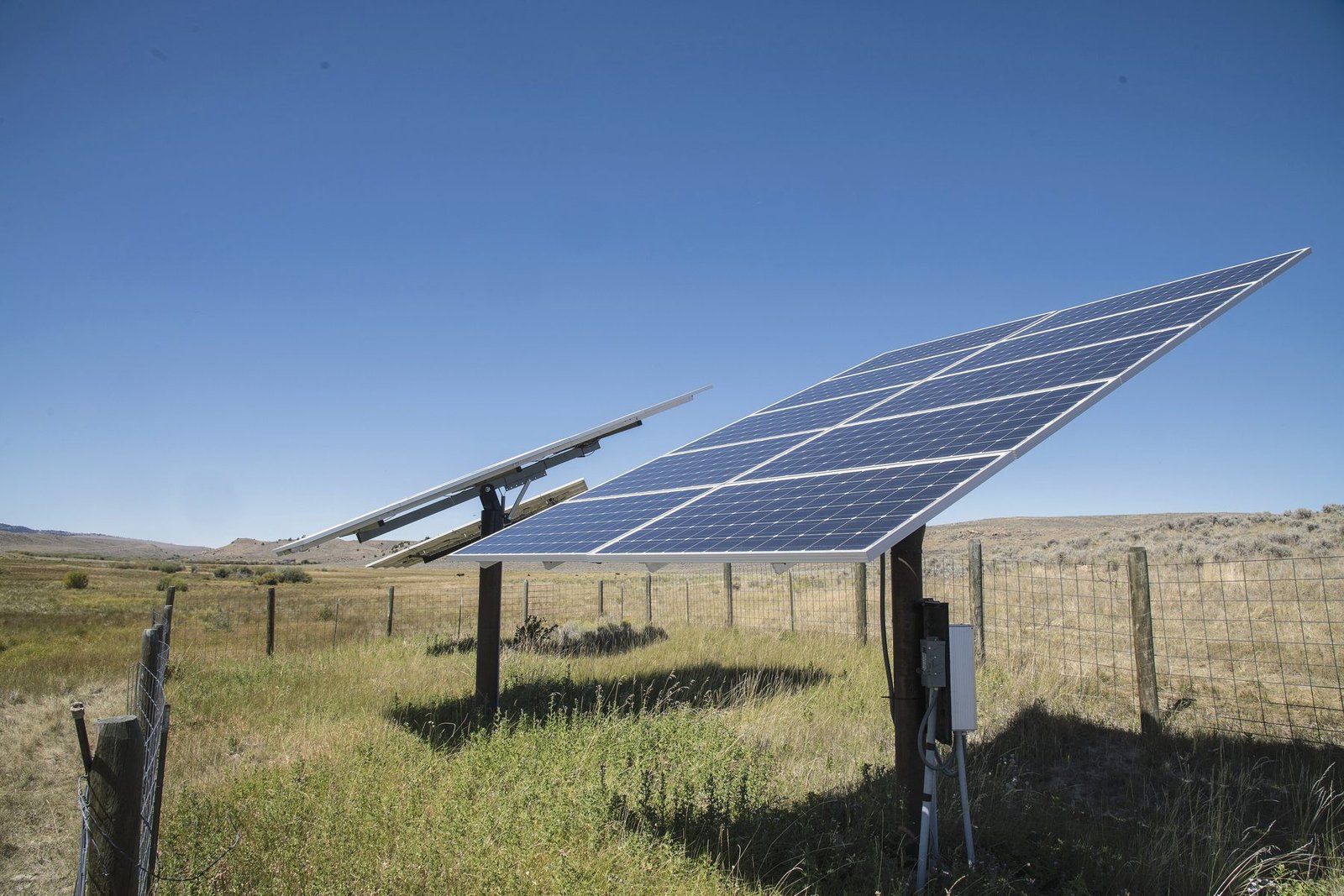 Solar panels on a steel frame inside a fenced pasture, powering a remote pump