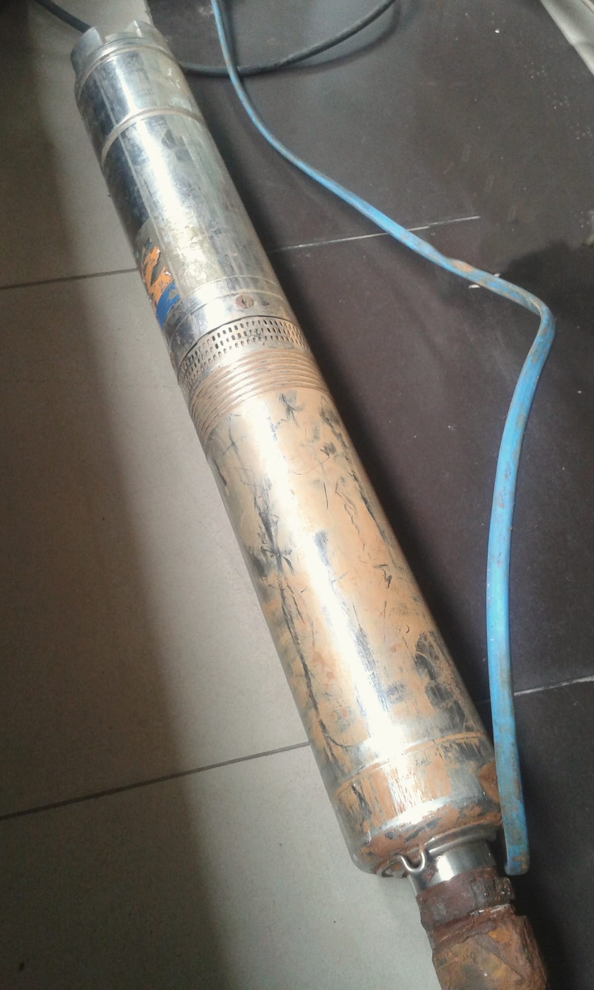A stainless steel submersible well pump with its blue cable, lying on a floor