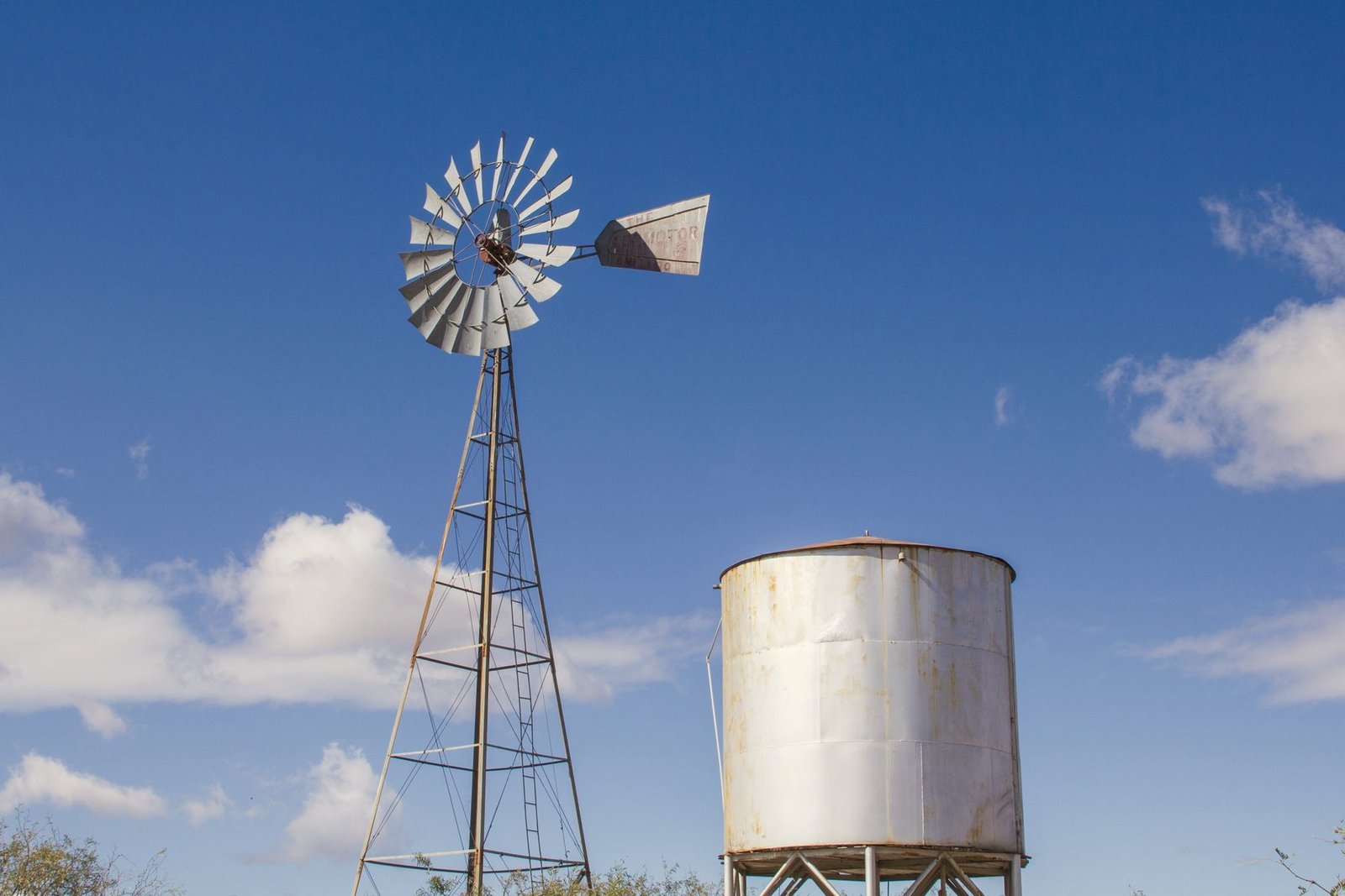 A windmill next to a white steel water storage tank against a blue sky with clouds