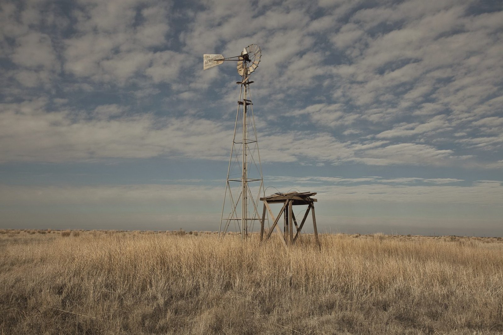 A windmill and wooden tank stand in tall dry grass under a mottled sky